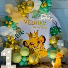 A vibrant Lion King "Wild One" birthday setup featuring a crowned Simba on a circular backdrop. The decor is accented with a "Happy Birthday" neon sign, a large light-up number '1', and an organic balloon garland in gold and green tones.