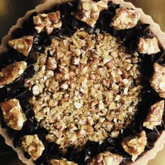 A slightly different angle of the dark chocolate and almond praline tart, showing the texture of the crushed nuts and the glossy finish of the chocolate.