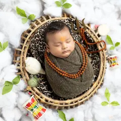 This top-down view shows the complete setup, with the baby nestled in a basket on a bed of clouds, surrounded by belpatra leaves, a shankha, and other divine elements.