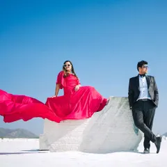 A stylish, editorial shot of the couple posing in a striking white landscape. The bride's vibrant red dress creates a stunning pop of color against the minimalist background.