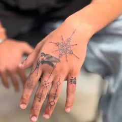 An intricate fine-line tattoo designed for the hand. This piece combines a swallow, symbolizing travel and freedom, with a geometric mandala and other small, meaningful symbols.