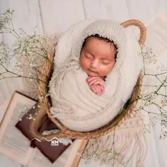 So peaceful and pure. This classic newborn shot features a beautifully swaddled baby in a simple basket, adorned with delicate baby's breath for a timeless look.