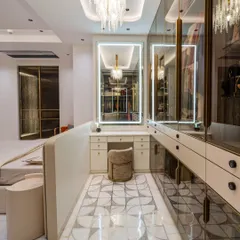 A full view of the walk-in closet, showcasing the stunning crystal chandelier, the glass-fronted wardrobes with gold trim, and the beautiful geometric-patterned floor inlay.
