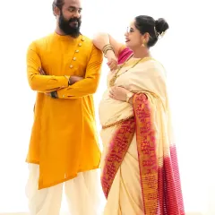 A stylish and traditional couple's portrait. The mom-to-be's elegant saree and the dad-to-be's bright kurta create a beautiful contrast against the minimalist white background.