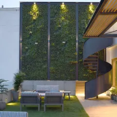 The terrace garden of the Screen House is an inviting retreat with a lush green wall. A striking spiral staircase acts as a sculptural centerpiece, elegantly connecting the garden to a smaller terrace above.
