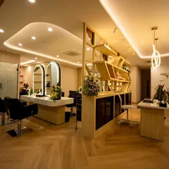 An overview of the salon's interior, showing the reception desk, the unique wooden partition shelf, and the main styling area. The design uses a mix of natural wood tones, soft lighting, and a floral wall mural to create a welcoming first impression.