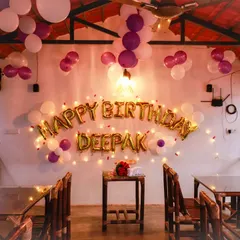 This restaurant birthday setup for Deepak features a "Happy Birthday" balloon banner accented with fairy lights and a purple and white balloon theme, instantly making the space feel special.