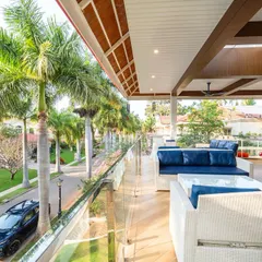 A view from the villa's expansive balcony, overlooking a street lined with palm trees. The crisp white wicker furniture with deep blue cushions offers a luxurious space for relaxation.