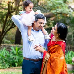 A happy family portrait taken in a park, with the daughter sitting on her father's shoulders.