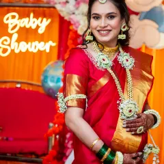 The radiant mom-to-be at her baby shower. She is glowing in a beautiful red and gold saree, adorned with traditional floral jewelry.