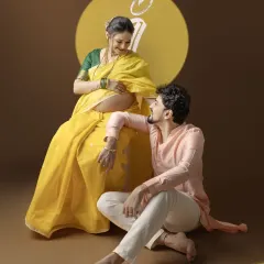 The couple shares a loving look during their traditional maternity session. The vibrant yellow saree and the 'Maa' projection create a visually stunning and meaningful composition.