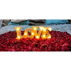 A close-up of a classic romantic detail for a "Just Married" room. A large heart made of red rose petals with a lit-up "LOVE" marquee sign placed in the center on the bed.