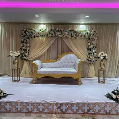 A classic and elegant stage for an engagement or reception. The setup includes a white and gold sofa, a backdrop of cream drapes, and a beautiful white floral arch.