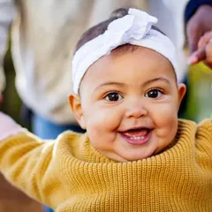 That big, gummy smile is just the best. This close-up captures the pure happiness of a baby who is learning to stand with a little help.