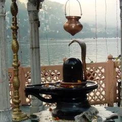A Shiva Lingam installed by a tranquil lake, merging the elements of water and earth in worship. I guide you on how to connect with the five elements through devotion to Lord Shiva.
