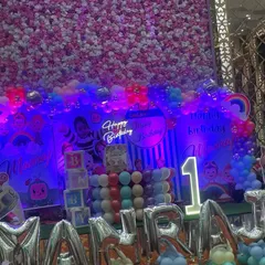 The Cocomelon birthday stage seen under vibrant party lights. The neon sign and colorful balloons pop under the purple and blue lighting, showing how the decor looks great both in daylight and during the evening celebration.