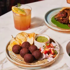 A plate of our signature small bites, perfect for a mid-week craving. These deep-fried savory balls are served with crispy potato wafers, a fresh tomato-onion salsa, and a vibrant green chutney.