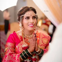A beautiful over-the-shoulder shot of the bride with her hands in a respectful 'namaste'. Her expression is full of warmth and anticipation, captured during the wedding ceremony.