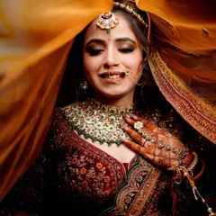 A classic "ghoonghat" shot. The bride's shy smile is beautifully captured through the veil, highlighting her intricate jewelry and the delicate details of her look.