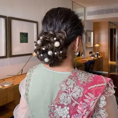 A messy bun decorated with dispersed pearls of various sizes. This is a modern and chic take on a classic updo, perfect for a cocktail party or reception.