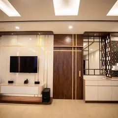 A modern living area where the TV unit is complemented by a stylish wooden partition and a mirrored crockery unit. The gold inlay details and strategic lighting add a touch of glamour and sophistication.