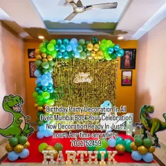 A roaring dinosaur-themed birthday party for Harthik. This setup includes a green and blue balloon arch, large T-Rex cutouts, and marquee letters spelling out the birthday boy's name.