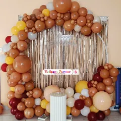 A birthday setup with a warm, earthy color palette of brown, yellow, and white balloons, set against a silver shimmer curtain for a festive backdrop.