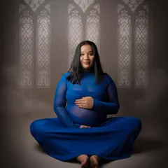 A serene, seated yoga pose where the mother-to-be cradles her bump. Her direct gaze and calm smile create a powerful connection with the viewer, radiating peace and confidence.