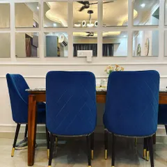 A closer view of the dining set, showing the quilted detailing on the blue velvet chairs and the elegant gold-tipped legs. These details, combined with the reflective quality of the mirror wall, contribute to the room's luxurious and contemporary feel.