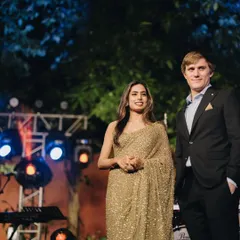 A candid moment from a client's cocktail event. The groom looks sharp in a classic black suit, a timeless choice that perfectly complements his bride's shimmering gold saree.