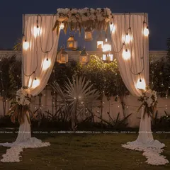 A wider view of the romantic bohemian arch, showcasing its placement on a lush green lawn, making it an ideal focal point for an outdoor evening event.