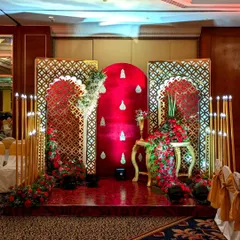 A regal photo corner for a reception, featuring a rich red velvet backdrop, ornate golden lattice screens, and cascading red floral arrangements.
