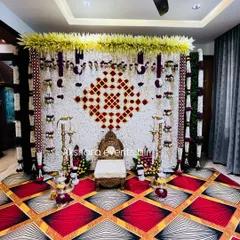 A beautiful backdrop for a Haldi or Sreemantham ceremony, made from a wall of white flowers with a geometric pattern in red. The decor is accented with hanging garlands and traditional lamps.