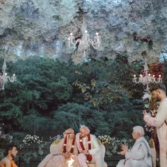 A couple shares a smile during their ceremony, seated under a magical ceiling of white flowers that feels like a cloud. We designed this space to feel like an enchanted forest, creating a warm and beautiful setting for their union.