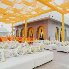 A bright and cheerful outdoor seating area for a Haldi, with white lounge sofas accented by custom-printed floral cushions and yellow draped ceilings.