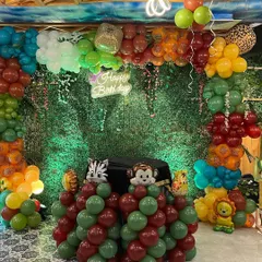 The full view of the jungle party backdrop, with a 'Happy Birthday' neon sign and a colorful balloon arch.
