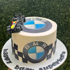 A custom cake for a superhero who loves cars. This BMW-themed cake features the iconic logo, a checkered flag pattern, and a toy race car on top.