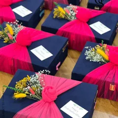 The combination of royal blue suede boxes and vibrant pink fabric wrapping creates a stunning visual contrast. Topped with dried flowers, these gifts are designed to make a bold and beautiful statement for any occasion.
