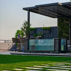 A daytime view of a stunning glass-walled pool with an integrated rain shower feature, set against a backdrop of a vertical garden. This is luxury and relaxation combined.