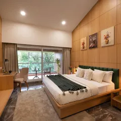 We design serene master suites that connect with the outdoors. This room features a custom wooden bed frame, a full-length wood-paneled accent wall, and sliding glass doors that open onto a private balcony with a lush, green view.