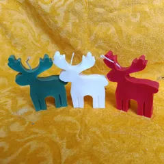 These reindeer-shaped candles in green, white, and red are a whimsical and fun decoration for the Christmas season.