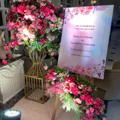 A beautiful welcome easel for a Roka ceremony, adorned with lush arrangements of pink flowers, setting a warm and inviting tone for the event.