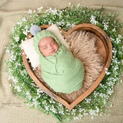 Dreaming in a wreath of love. This sweet baby is nestled in a heart-shaped bowl, surrounded by a halo of baby's breath, creating a pure and angelic portrait.