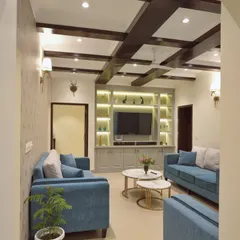 For this homestay in Dehradun, we designed a cozy yet refined living area. The coffered ceiling features a structural beam cladded in exquisite veneer, which we balanced with a second, identical beam. The design combines a muted color palette with vibrant teal sofas for a welcoming feel.