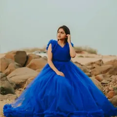 A solo portrait of a client in our royal blue ruffled gown, set against a rocky, natural landscape.