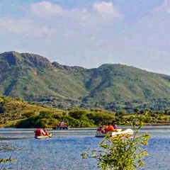 A scenic view of people kayaking and boating on a lake surrounded by the Aravalli hills in Udaipur. It's a relaxing way to spend the day and take in the stunning natural landscape.
