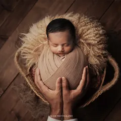A tender close-up of a newborn, swaddled and held securely in their father's hands. This image highlights the delicate details and profound sense of safety in those first few days.
