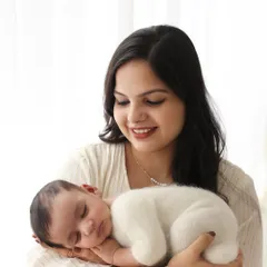 A beautiful solo portrait of a mother cradling her newborn. The baby is snug in a soft, fuzzy white outfit, emphasizing their newness and innocence.