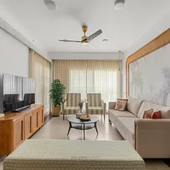 This living room in a Shobha Windsor apartment shows how simplicity can be full of soul. We solved the lack of a TV wall by creating a custom feature wall that integrates the TV unit and a Mandir, framed by beautiful cane detailing and monochromatic wallpaper.