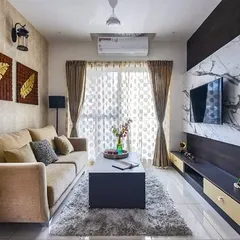 A cozy living room setup featuring a dark wood media unit with a striking white marble-patterned laminate backdrop. The warm tones of the curtains and sofa create an inviting space for family movie nights.